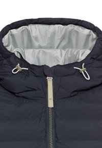 Marineblauwe pufferjas met een gevoerde, trekkoordkap, een ritssluiting aan de voorkant en een grijze voering aan de binnenkant. Voorzien van toggle-connectoren en een gequiltde textuur.