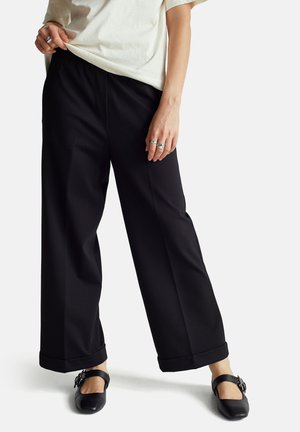 Zwarte wijde pantalon met een zachte textuur en een opgevouwen zoom. Gekocht met een crèmekleurig bovenstuk en zwarte platte schoenen met decoratieve hardware.
