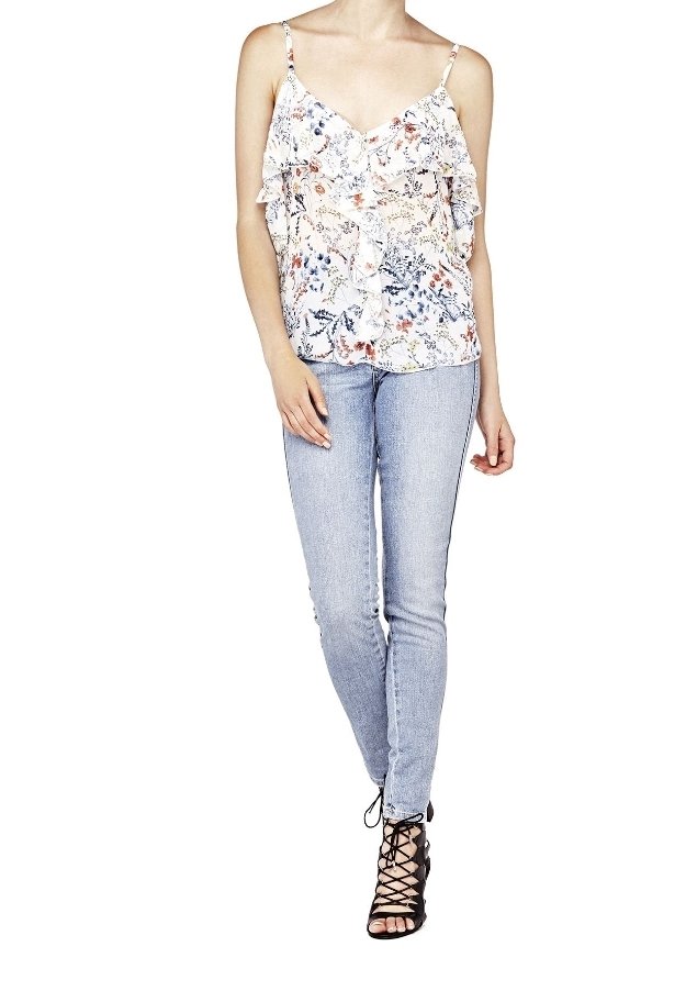 Femme portant un top blanc à volants sans manches à motif floral, un jean skinny bleu clair et des sandales noires à talons hauts et à lacets.