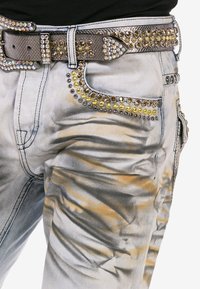 Denim-Jeans mit einem grauen und gelben Farbverlauf. Mit metallischen Nieten entlang der Taschen und einem mit Nieten versehenen silbernen Gürtel mit strukturierten Akzenten.