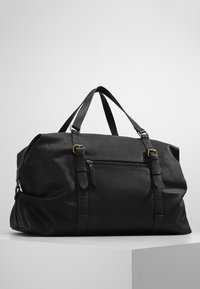 Bolso de viaje de piel negra con dos asas superiores, bolsillo frontal con cremallera y herrajes en tono dorado. Superficie texturizada y diseño espacioso.