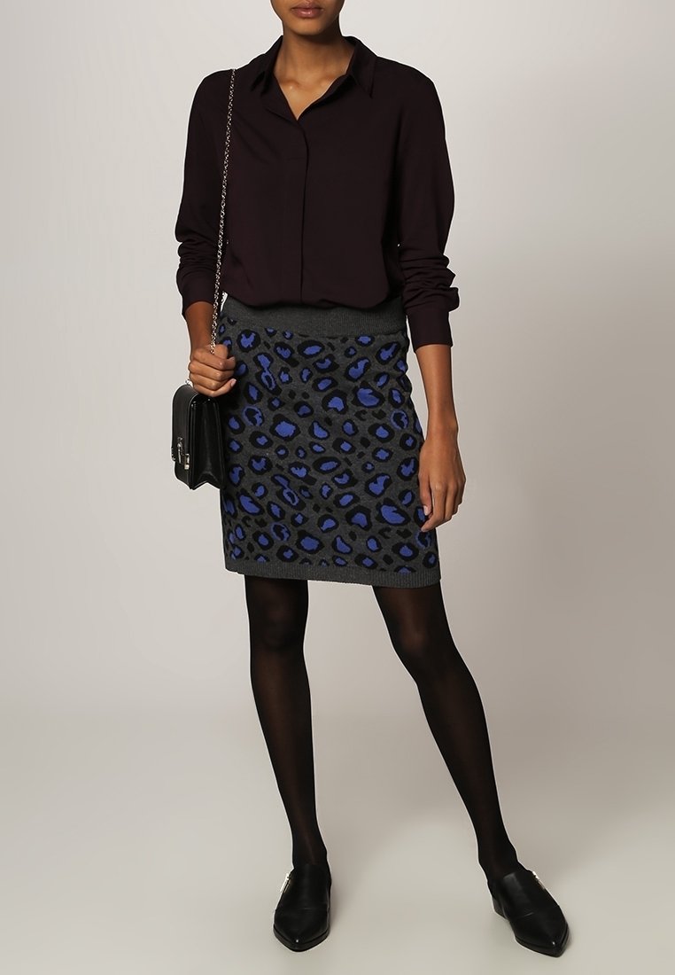 Camicia a maniche lunghe viola scuro abbinata a una gonna grigia con stampa leopardata blu. Il modello indossa collant e scarpe neri, mentre tiene una borsa nera.