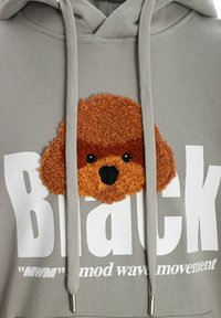 Sudadera gris con una cara de perro de peluche marrón texturizada. Grandes letras blancas que dicen "Black", con "MWM" y "mod wave movement" debajo.