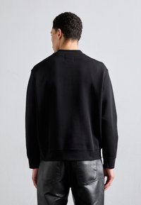 Black sweatshirt made of soft material, featuring a crew neck, ribbed cuffs, and a relaxed fit, paired with black, shiny leather pants.