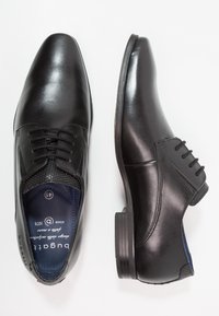 Zapatos de vestir de cuero negro con un acabado suave, punta afilada y diseño de cordones. Paneles laterales texturizados, suela de goma e interior azul marino.