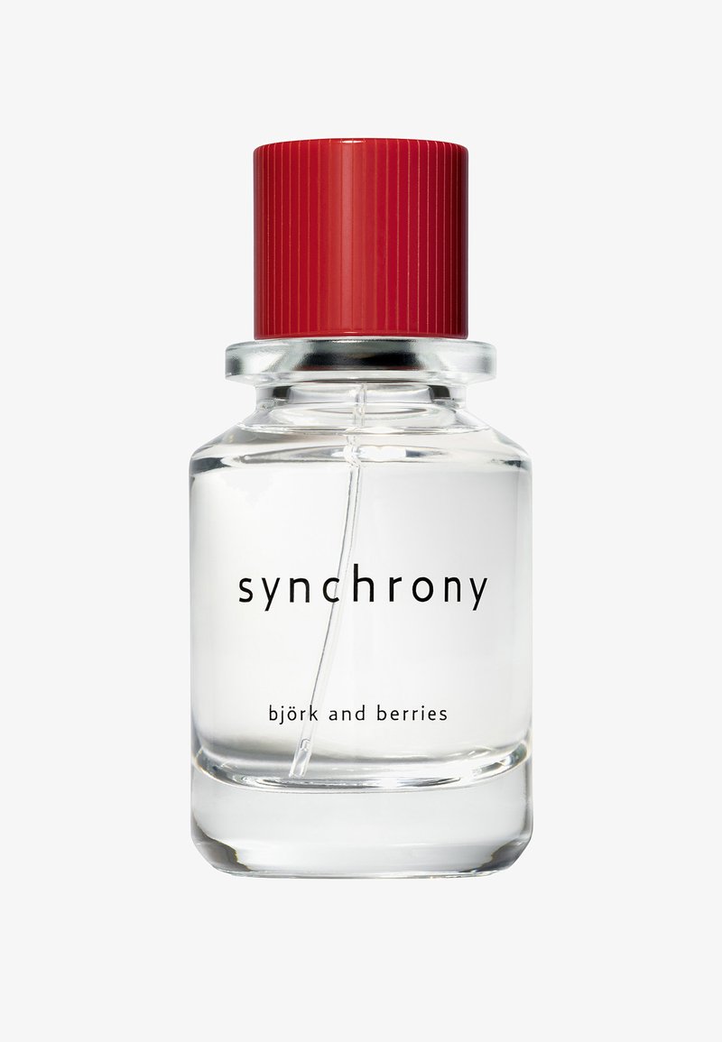 Clear glass perfume bottle with red cap labeled "synchrony" and "björk and berries" showing liquid and spray tube inside.