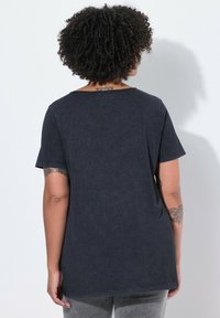 T-shirt en coton bleu foncé à manches courtes, avec un col rond, une coupe décontractée et des accents de couture visibles. La vue arrière montre une texture lisse.