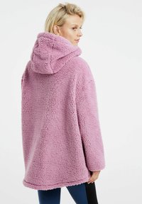 Cappotto sherpa rosa con cappuccio, vestibilità oversize, tessuto testurizzato e tasche laterali. Orlo liscio e maniche lunghe, che offrono calore.