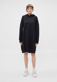 Čierne šaty s kapucňou vo forme mikiny, s voľným strihom a dlhými rukávmi. Na prednej strane vyšívané logo "Marc O'Polo" v tmavomodrej farbe.