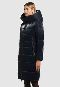 Cappotto puffer navy con finitura lucida, colletto alto, maniche lunghe e tasche laterali con zip. Presenta un motivo a righe orizzontali e il logo del marchio sulla manica.