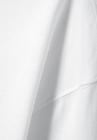 Bílá bavlněná látka s hladkou texturou a jemným prošitím. Obrázek se zaměřuje na detailní pohled na materiál a šev.