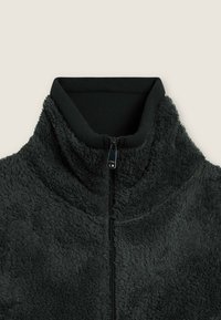 Giacca in pile nera con colletto alto, zip completa e superficie testurizzata. Il colletto interno è a coste, aumentando comfort e calore.
