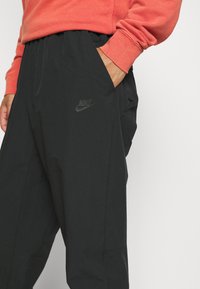 Černé kalhoty s volným střihem, vyrobené z lehkého materiálu. Obsahují boční kapsy a tónové logo Nike na stehně.