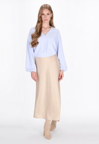 Lyseblå bluse med lange ærmer, v-udskæring og beige maxiskirt. Glat stoftekstur, brugt med beige hæle støvler til anklerne.