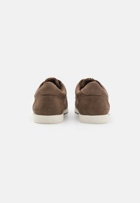 Zapatillas de cuero marrón con una textura suave, suelas de goma blanca y acentos de costura mínimos. Presentan un diseño de corte bajo con una paleta de colores básica.