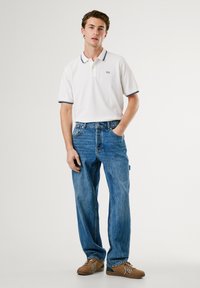 Hvit polo skjorte med marineblå ribbestrikket krage, brodert logo, kombinert med lyseblå rette jeans og brune sko. Enkel, casual stil.