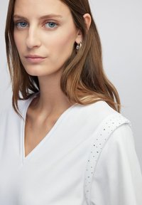 Witte V-hals top met korte mouwen, met glanzende strassaccenten op de schouder. Zachte stof met een gladde textuur.