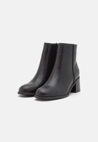 Bottines noires en simili cuir lisse, dotées d'une forme effilée, d'un talon carré et de détails de coutures latérales minimalistes.