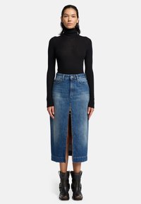 Jupe midi en denim bleu avec un détail de fermeture éclair à l'avant, taille haute et décoloration subtile. Associée à un col roulé noir côtelé et des bottines noires.