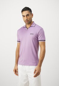 Levandų polo marškinėliai su juodais akcentais, trumpomis rankovėmis ir apykakle. Yra vertikalios juostelės ir mažas "BOSS" logotipas ant krūtinės.