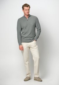Grau zipfelpulli aus weichem Stoff mit gerippten Bündchen, kombiniert mit cremefarbenen Hosen und beigen Sneakers. Einfaches, modernes Design.