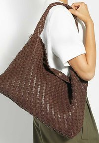 Brown woven tote bag with a textured finish and a slouchy design. It features a shoulder strap and a decorative button closure.