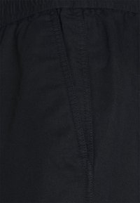 Gros plan sur un tissu noir avec une taille élastique et une poche verticale sur la couture latérale d'un vêtement.