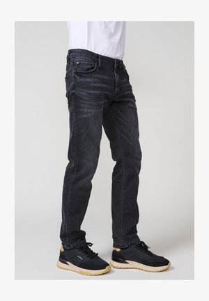 Jeans de denim albastru închis, cu un croi slim, design cu cinci buzunare și ușoare semne de uzură. Asortați cu pantofi sport negri cu o talpă ușoară.