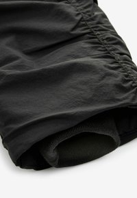 Schwarzes Textilkleidungsstück mit einem gerafften Design, glatter Textur und einer gefalteten Partie, die ein kontrastierendes dunkelgrünes, geripptes Innenfutter zeigt.