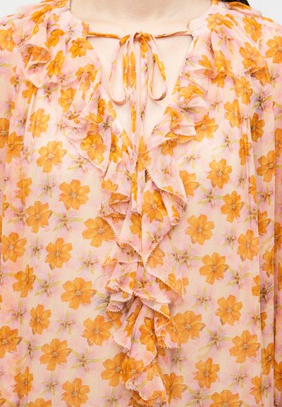 Διάφανη ροζ μπλούζα με πορτοκαλί λουλουδάτο σχέδιο, με βολάν μπροστά και δεμένη φιόγκο στο λαιμό.