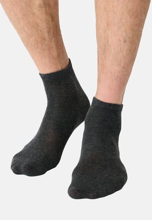 Calcetines negros hasta el tobillo hechos de un material suave y elástico con un puño acanalado. Presentan una textura lisa y un diseño estándar en la puntera.