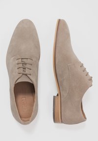 Chaussures en daim taupe avec une toe arrondie, un design à lacets à quatre œillets, une semelle en cuir et un accent de talon en bois. Texture lisse dans l'ensemble.
