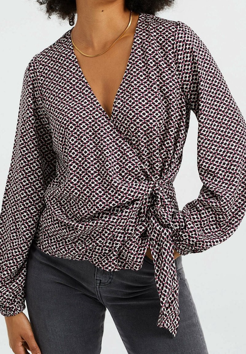 Blouse portefeuille en tissu à motifs aux tons bordeaux et blancs. Manches longues avec poignets froncés, nouée à la taille.