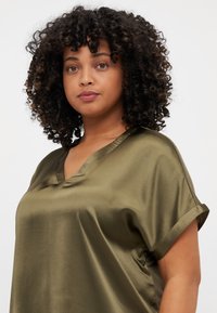 Blusa di raso verde oliva con maniche corte arrotolate e scollatura a V, caratterizzata da una texture liscia e una vestibilità comoda.