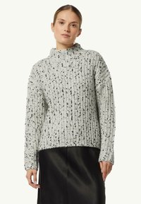 Helles graues Strickpullover mit hohen Kragen, der ein strukturiertes Muster und schwarze Sprenkel aufweist. Lange Ärmel und eine locker sitzende Passform.