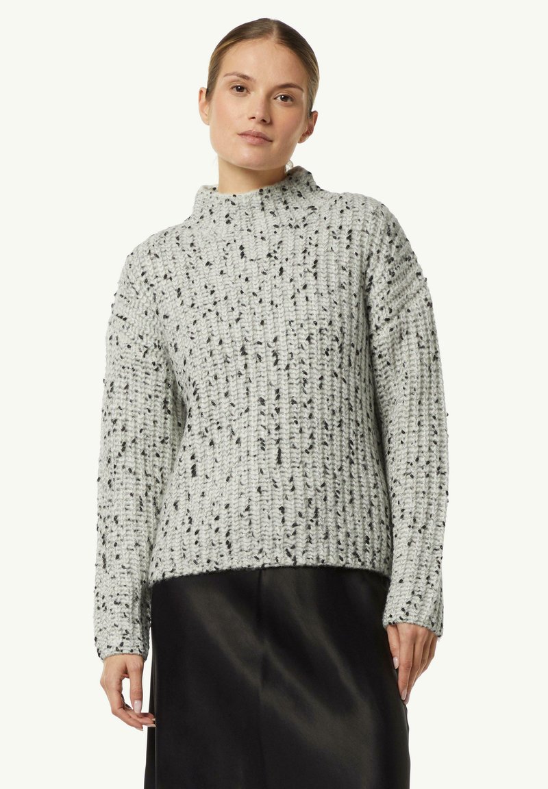 Helles graues Strickpullover mit hohen Kragen, der ein strukturiertes Muster und schwarze Sprenkel aufweist. Lange Ärmel und eine locker sitzende Passform.