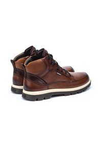 Botines de cuero marrón con cordones negros, cuello acolchado y suela de goma texturizada. Presenta detalles de cuero en contraste y una puntera redondeada.