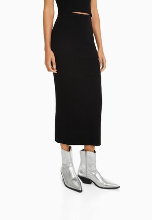 Falda midi de canalé negra combinada con botines de vaquero metálicos plateados que cuentan con punta afilada y cierre lateral.