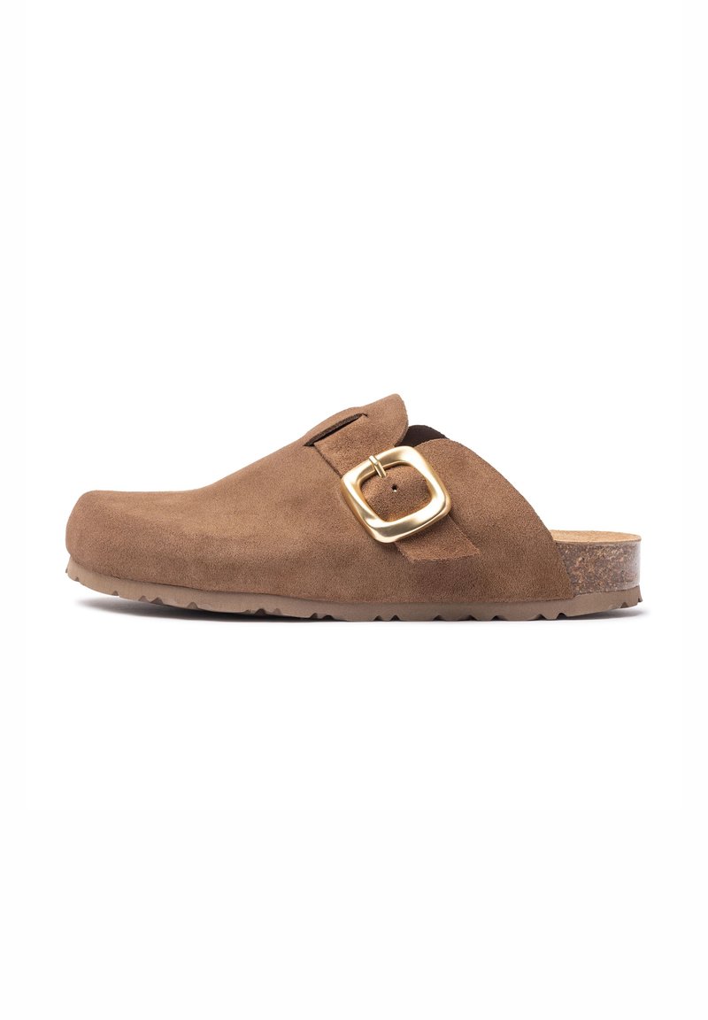 Sabot en daim marron avec un bout rond, une sangle ajustable et un détail en boucle dorée. Présente une semelle en caoutchouc texturée et foncée.
