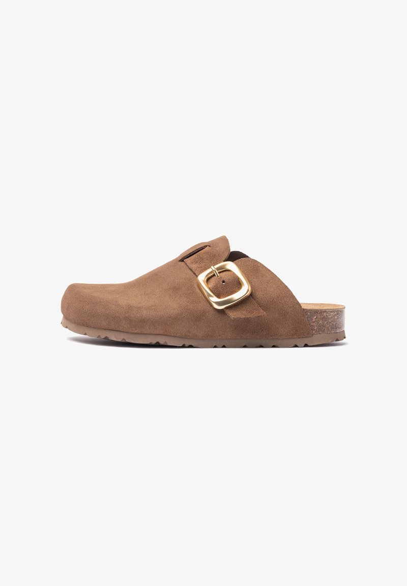 Sabot en daim marron avec un bout rond, une sangle ajustable et un détail en boucle dorée. Présente une semelle en caoutchouc texturée et foncée.