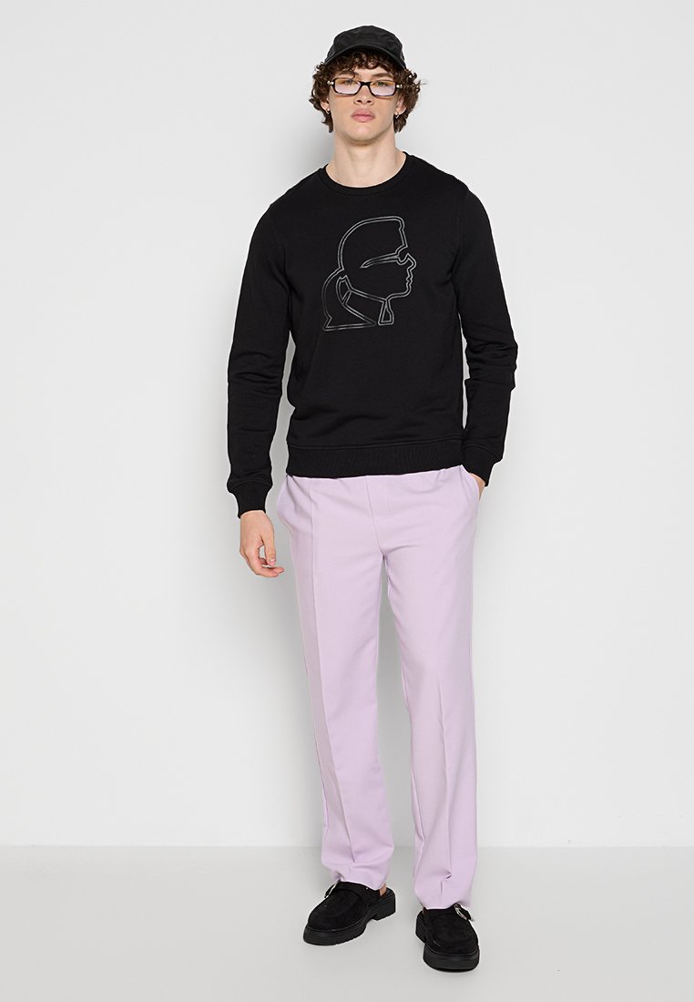 Sweatshirt noir avec un design graphique à contour fin sur le devant, assorti à un pantalon violet clair et des baskets noires.