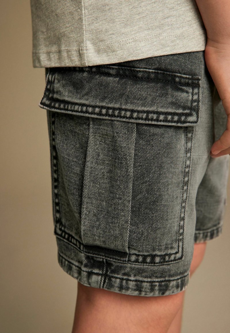 Los pantalones cortos de mezclilla gris tipo cargo cuentan con varios bolsillos, un corte holgado y costuras visibles. La textura es ligeramente desgastada, con una apariencia robusta.