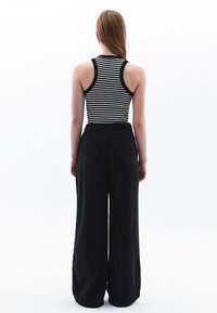 Zwarte wijdlopende broek met een relaxte fit en een gladde textuur, gecombineerd met een fitted zwart-wit gestreept tanktop.