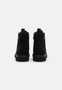 Stivaletti in suede nero con cerniere sul retro, suole in gomma piatta e dettaglio del logo in rilievo sul lato esterno.