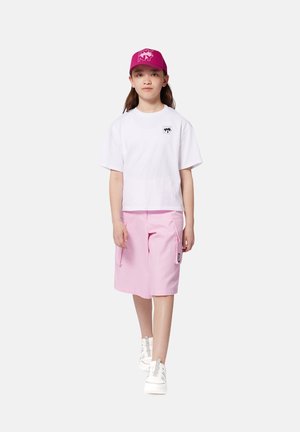 Witte cropped t-shirt met zwart logo, lichtroze cargo shorts met zijzakken, en witte sneakers. Roze pet met logo in gedetailleerd ontwerp.