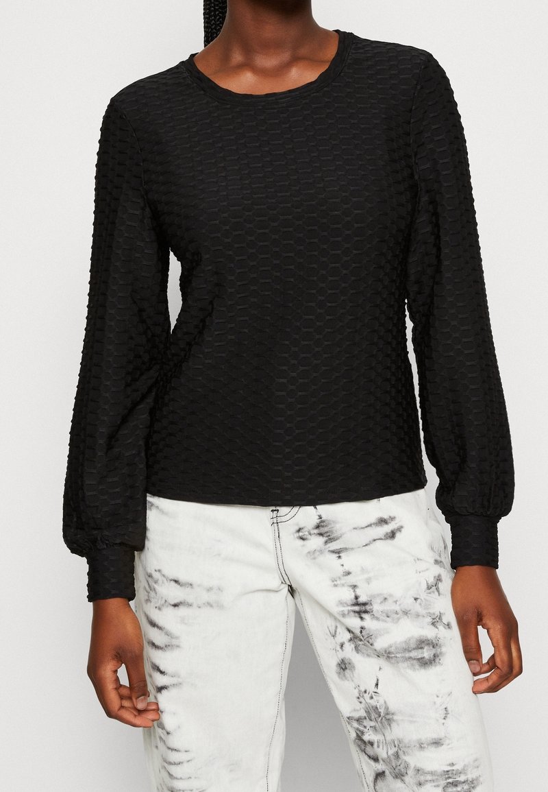 Top nero a maniche lunghe con motivo a nido d'ape testurizzato e scollo rotondo. Abbinato a jeans bianchi tie-dye con accenti neri.