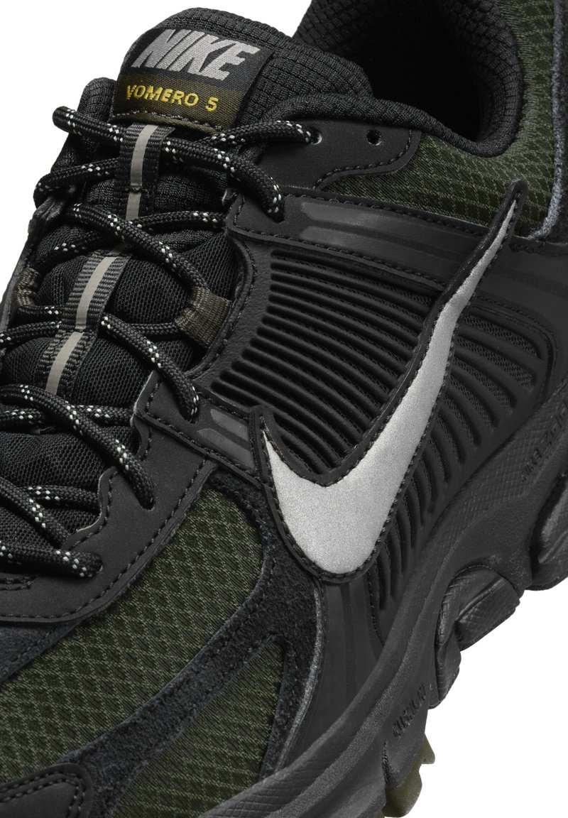 La sneaker Nike Vomero 5 présente un dessus en mesh noir et vert olive avec des accents texturés, un Swoosh argenté et des détails réfléchissants sur les lacets.