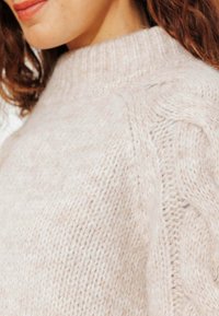 Pull en tricot rose clair avec un col côtelé haut et des motifs texturés, en matériau doux et pelucheux, avec une coupe décontractée.