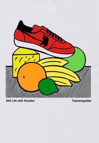 Červená sneakers s černými akcenty leží na žlutém sýru, obklopená oranžovým, zeleným a žlutým ovocem, na bílém pozadí.