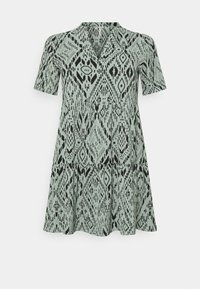 Sukienka z krótkim rękawem z jasnozielonej tkaniny z czarnym geometrycznym wzorem. Dekolt w serek i rozkloszowana spódnica z wielowarstwowym krojem.